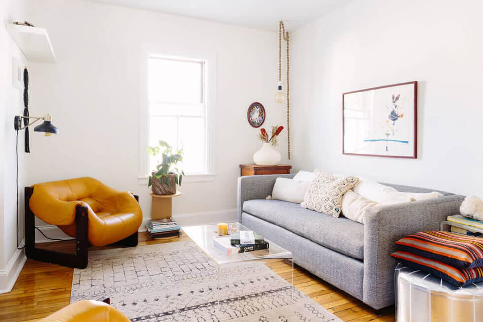 Cosy and eclectic white living room with grey sofa, patterned rug and camel armchairs.